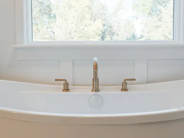 Freestanding tub faucet beneath the bathroom window with white paneled walls.