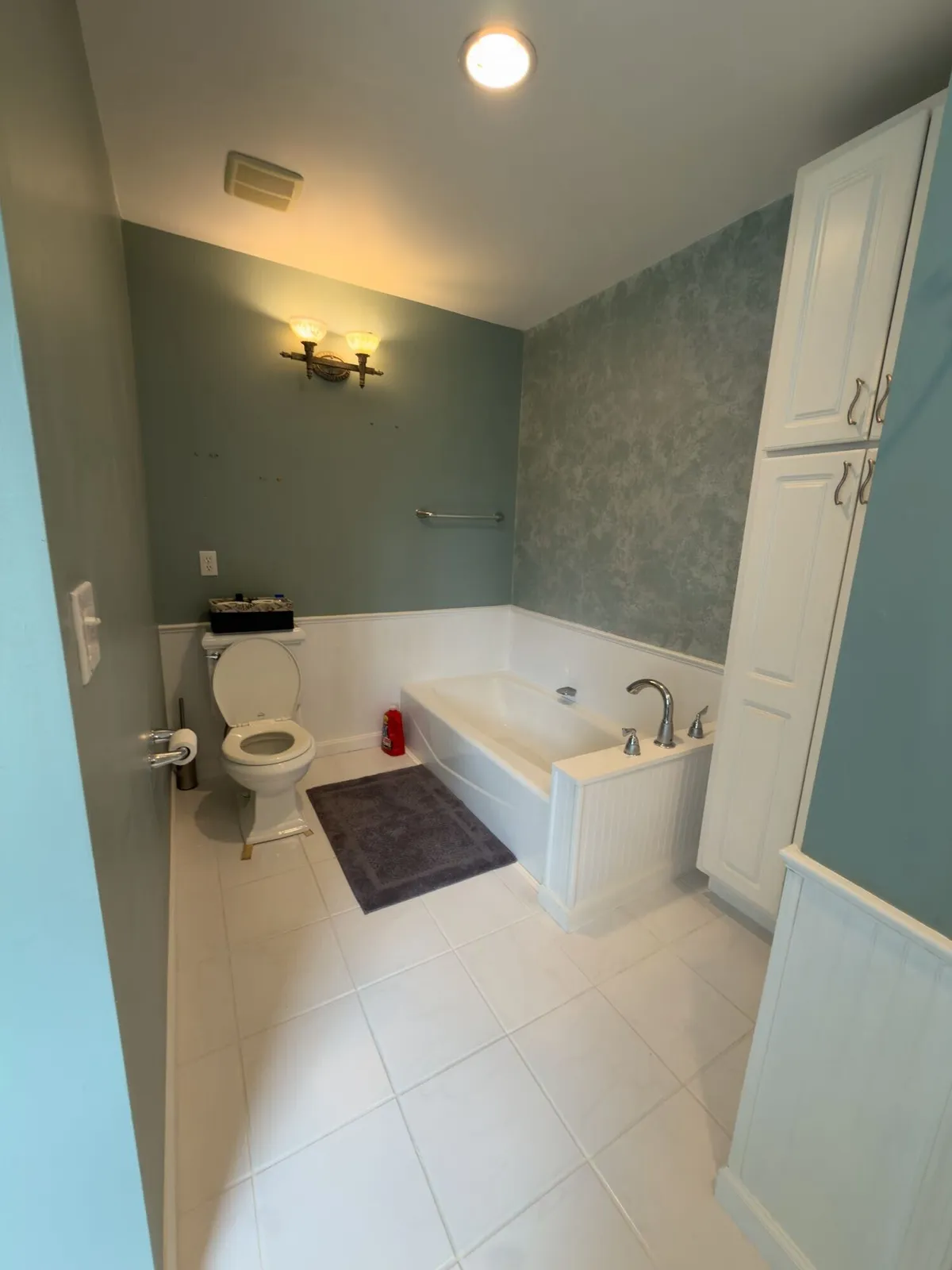 Before remodeling: Harrisburg bathroom with a built-in tub, paneled tub deck, blue-green textured walls, a tall white cabinet and white tile floor.