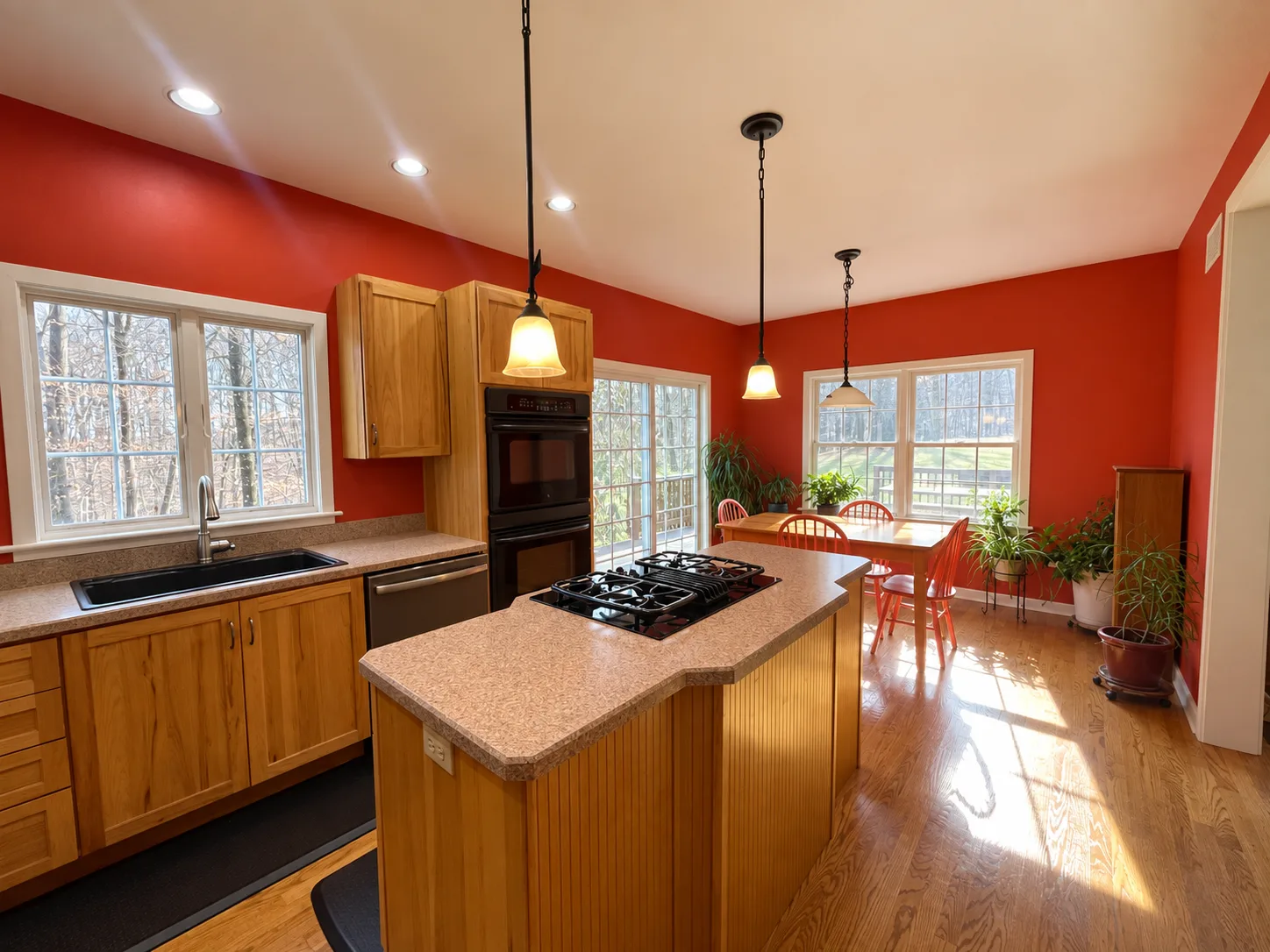 Before remodeling: Hershey kitchen with red walls, wood cabinets, a cooktop island, stacked black wall ovens and a dining table beside large windows.