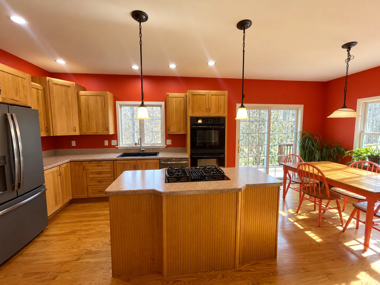 Before remodeling: wide view of the Hershey kitchen with wood cabinetry, beige countertops, an island cooktop and a dining table beside the sliding glass door.