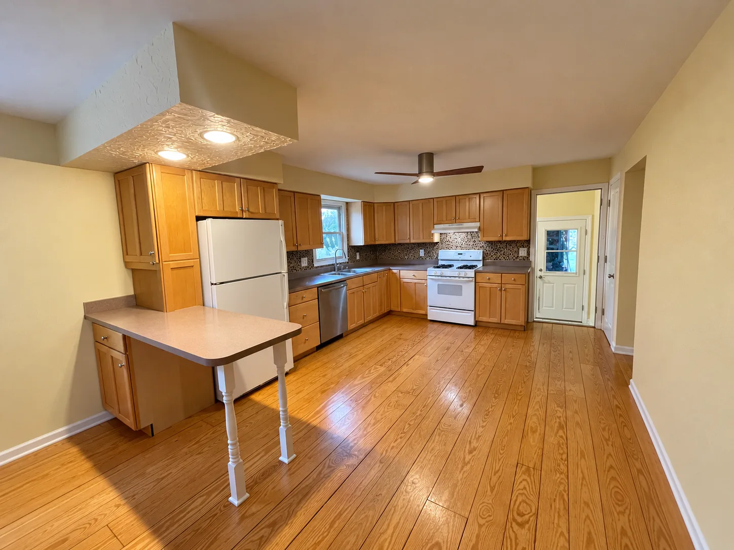 Before remodeling: Hummelstown kitchen with wood cabinets, brown counters, a narrow peninsula, white refrigerator and range, and a ceiling fan.