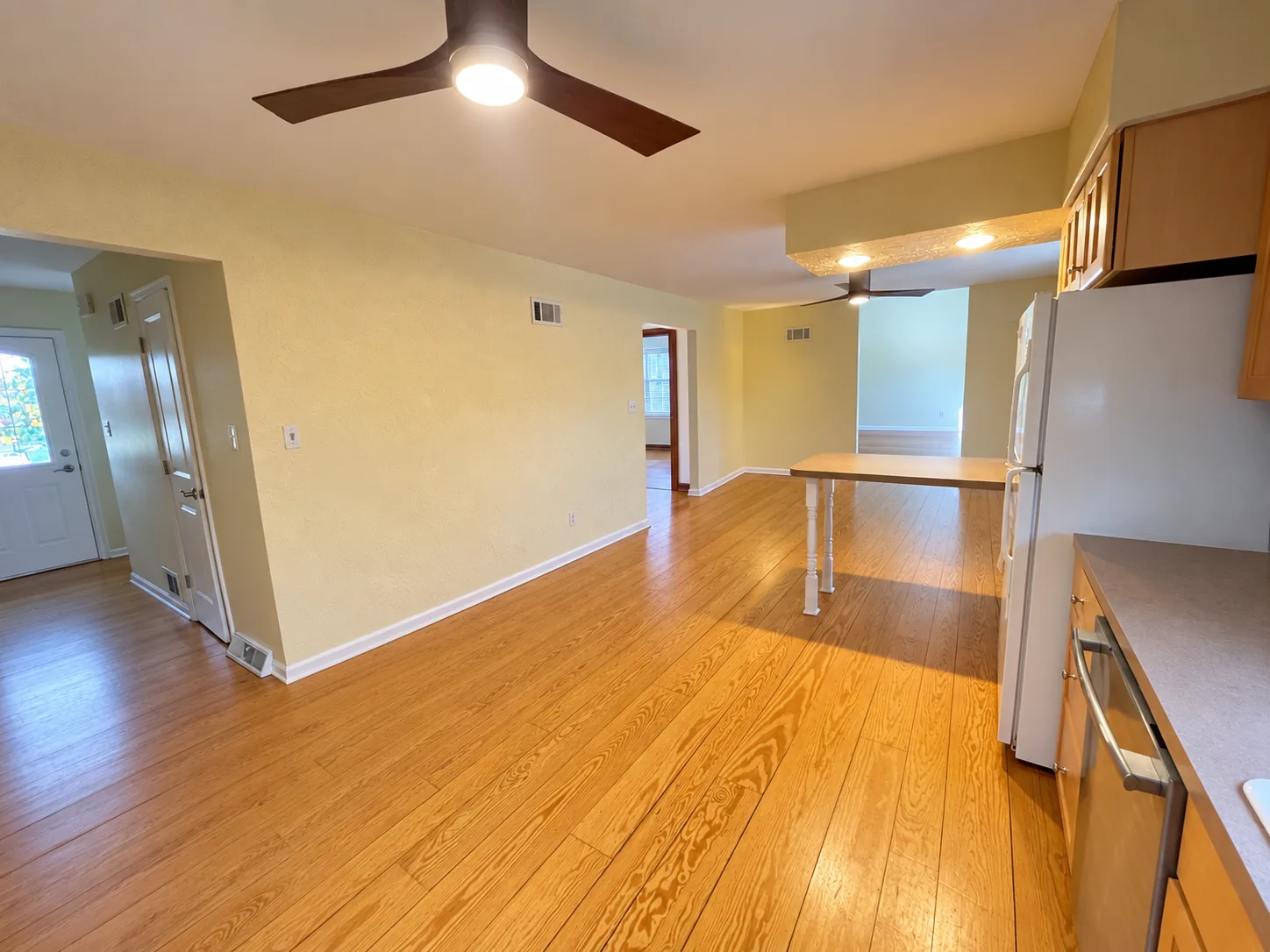 Before remodeling: view along the Hummelstown kitchen toward the peninsula and dining area, with a white refrigerator, ceiling fans and adjoining doorways.