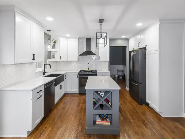 Wide view along the finished kitchen with an island wine rack, white cabinetry, black apron-front sink and dark refrigerator.