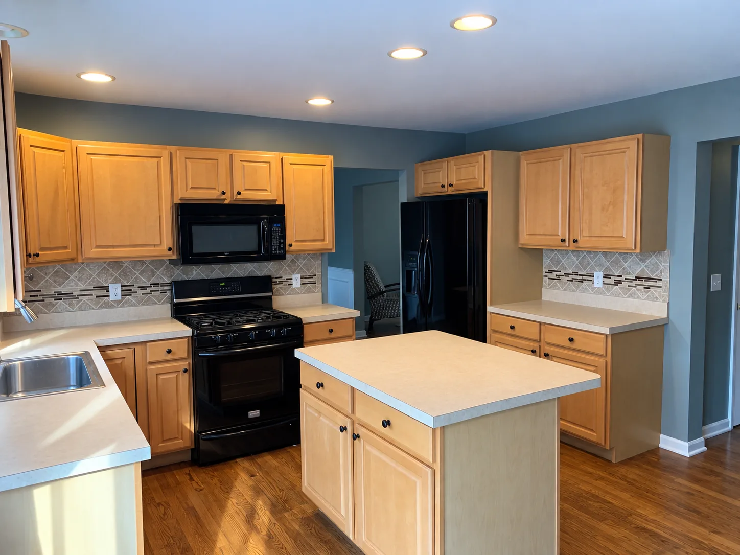 Before remodeling: Enola kitchen with wood cabinets, beige countertops, a wood island, black range and microwave, and a patterned tile backsplash.