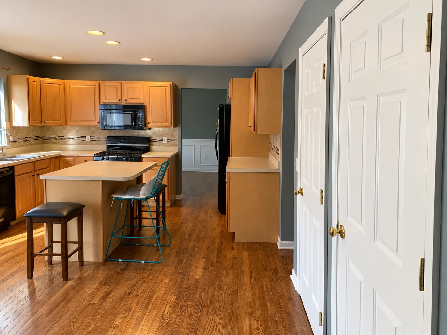 Before remodeling: Enola kitchen viewed beside two white doors, showing the wood island, stools, wood cabinetry and black appliances.