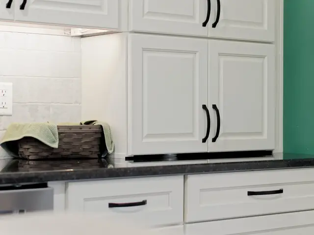 White storage cabinets with black pulls above a dark countertop beside the dishwasher and green accent wall.