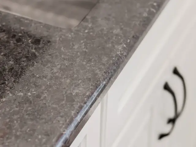 Detail of the dark countertop edge above white cabinet doors and black hardware.