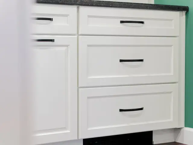 White base drawers with black pulls and a dark countertop beside the green kitchen wall.
