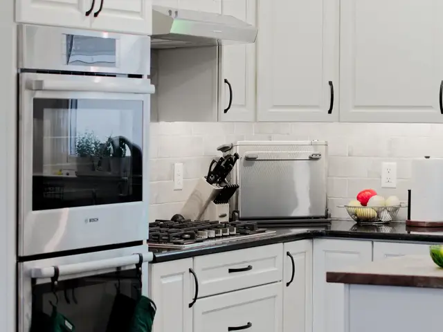 Kitchen viewed from the dining area, showing stacked ovens, the gas cooktop, white corner cabinets and the edge of the wood-topped island.