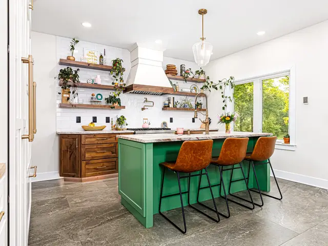 Finished kitchen overview with a green island, three woven stools, wood base cabinets, white tall cabinetry and floating shelves.