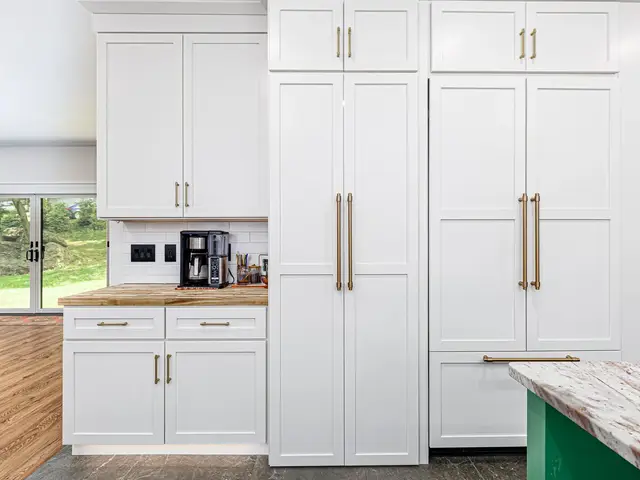 Tall white kitchen cabinets with gold-tone handles beside a window-side coffee counter.
