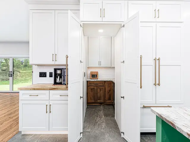 Open passage between tall white cabinets leading to a pantry with wood lower cabinetry.