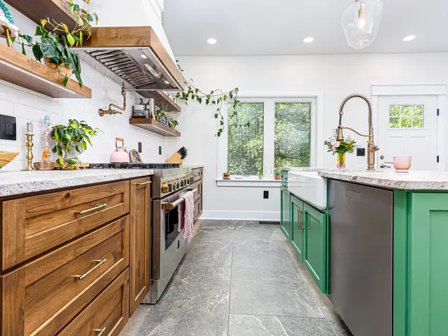 Kitchen walkway between wood base cabinets and a green island toward bright windows.