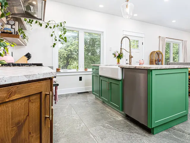 Green kitchen island with a stainless dishwasher, light countertop and tall faucet beside large windows.