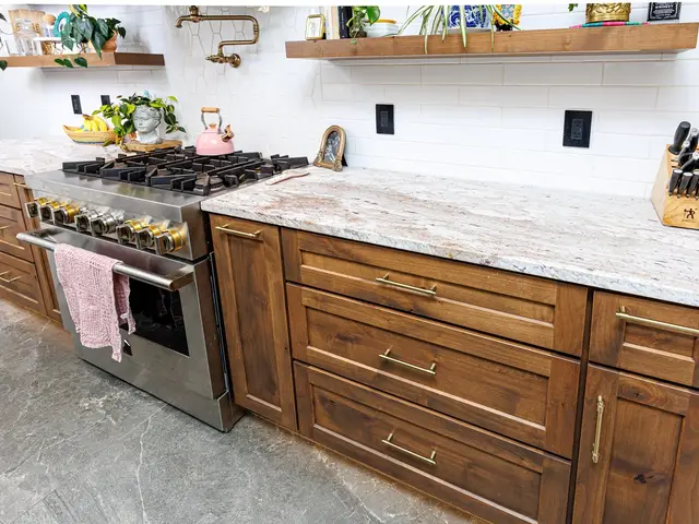 Angled view of the stainless gas range beside wood drawers and a light veined countertop.